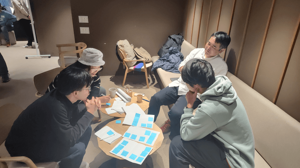 小さなテーブルを囲み、青い付箋を使ってアイデア書き出し議論しているチーム。