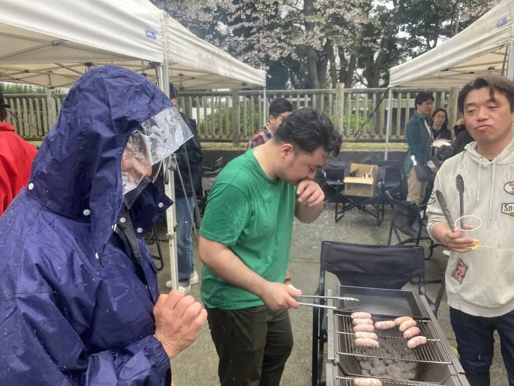 小雨の中BBQのお肉を焼いている社員達