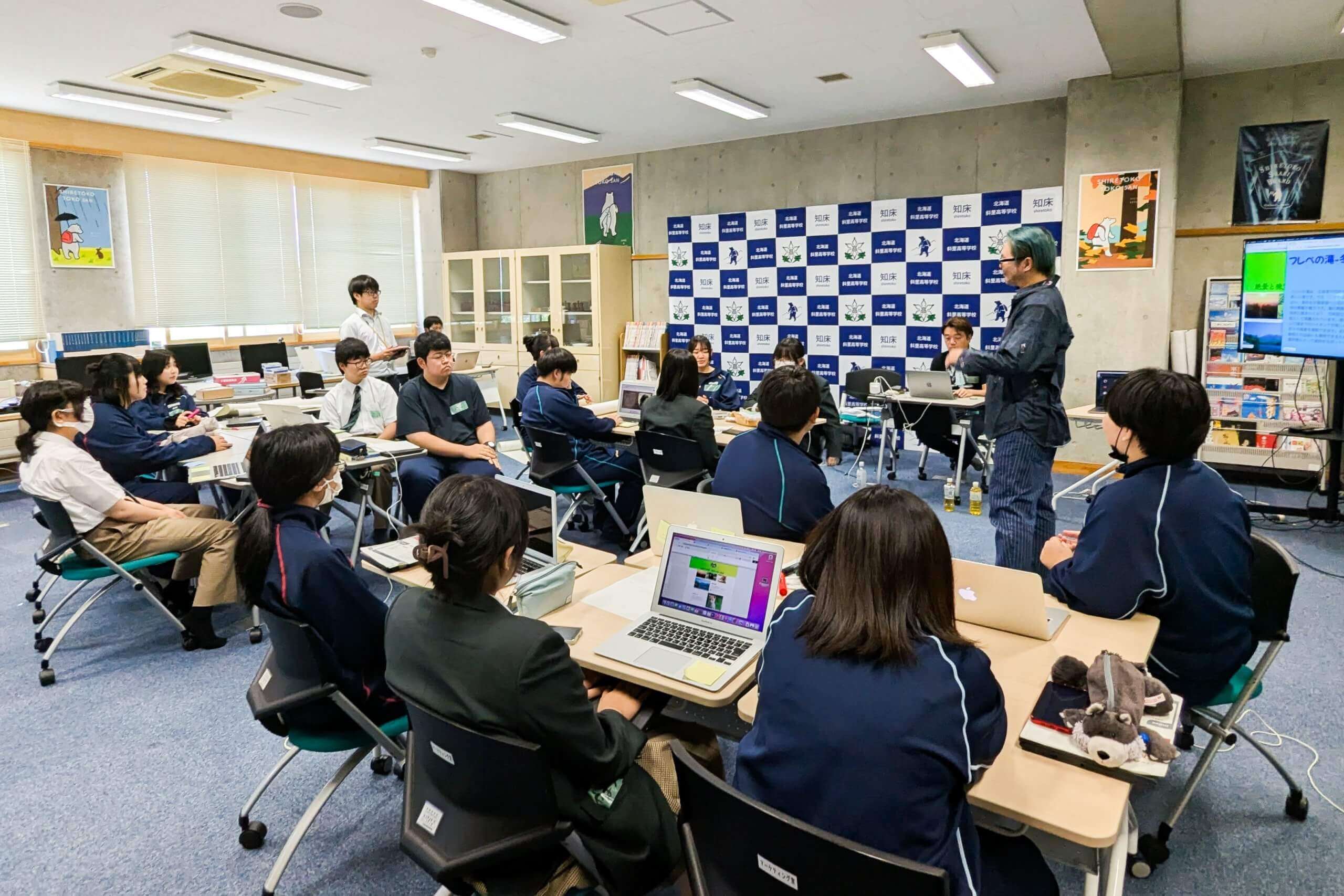 教室で机を並べた生徒たちの中で授業をしている写真