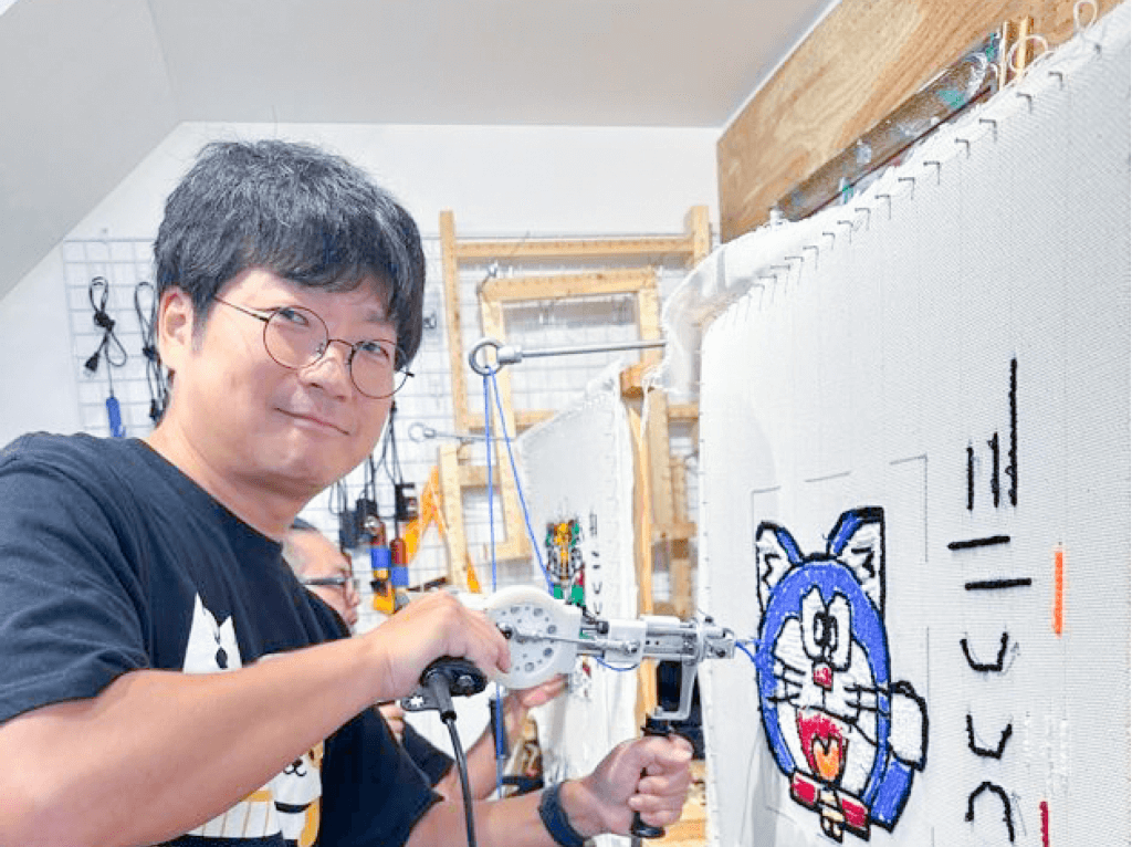 タフティングガンを使用してデザインに合わせて毛糸を布に打ち込んでいる部員の画像